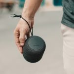 From above of crop anonymous male listening to music from modern portable speaker on pavement in city